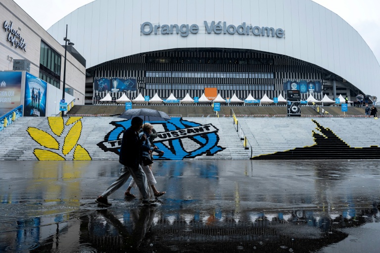 Des piétons abrités sous un parapluie passent devant le stade Vélodrome, où le match de L1 OM-PSG a été reporté de 24 heures en raison des intempéries, le 21 septembre 2025 à Marseille