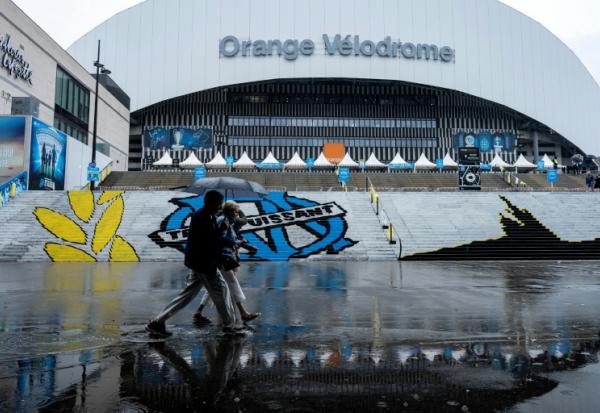 Des piétons abrités sous un parapluie passent devant le stade Vélodrome, où le match de L1 OM-PSG a été reporté de 24 heures en raison des intempéries, le 21 septembre 2025 à Marseille