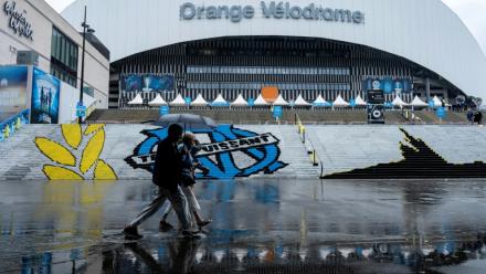 Des piétons abrités sous un parapluie passent devant le stade Vélodrome, où le match de L1 OM-PSG a été reporté de 24 heures en raison des intempéries, le 21 septembre 2025 à Marseille