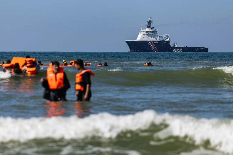 Des migrants tentent de monter à bord d'un bateau de passeurs au large de la plage d'Equihen-Plage, dans le nord de la France, tandis qu'au loin patrouille l'Abeille Normandie, remorqueur français d'urgence, le 23 septembre 2026