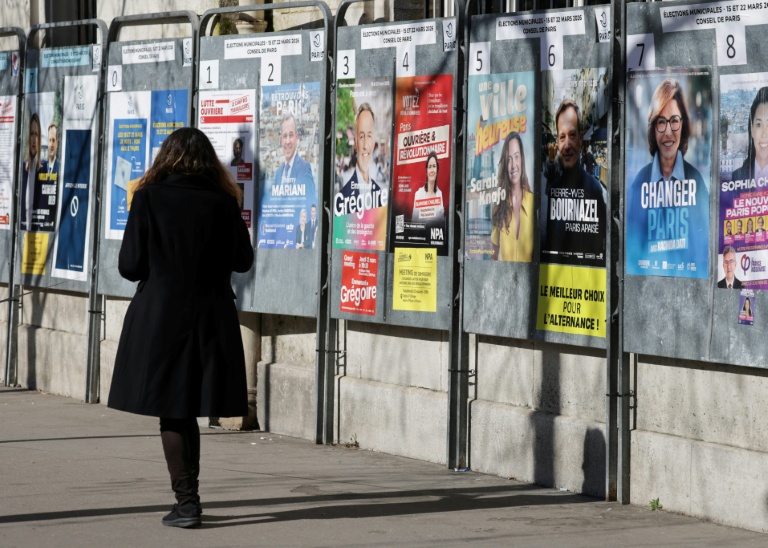 Une femme passe devant un panneau électoral avec les candidats à la mairie de Paris, le 9 mars 2026, à Paris