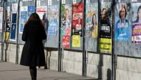 Une femme passe devant un panneau électoral avec les candidats à la mairie de Paris, le 9 mars 2026, à Paris