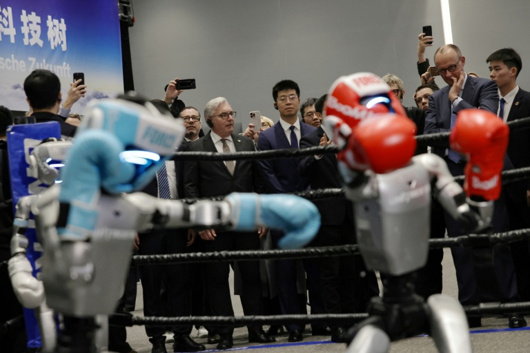 Le chancelier allemand Friedrich Merz (2e d) observe un combat de boxe entre deux robots humanoïdes dans une salle d'exposition des produits Unitree Robotics à Hangzhou, dans l'est de la Chine, le 26 février 2026 