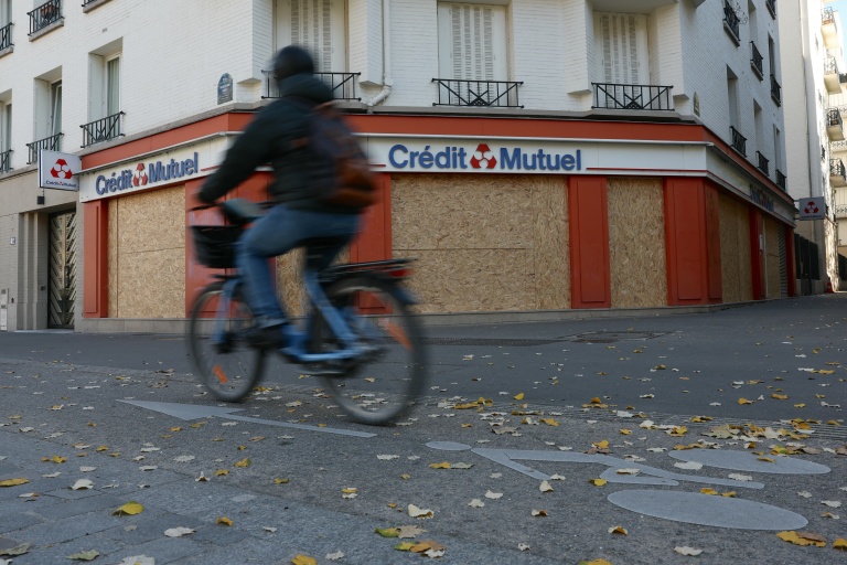 Un cycliste passe devant une banque barricadée par des plaques de bois à Paris le 30 octobre 2026