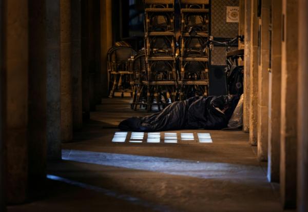 Un sans-abri dort dans un sac de couchage à côté de la terrasse d'un café à Paris, le 15 octobre 2025