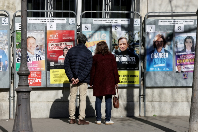 Des passants regardent les affiches électorales des candidats aux municipales à Paris le 9 mars 2026