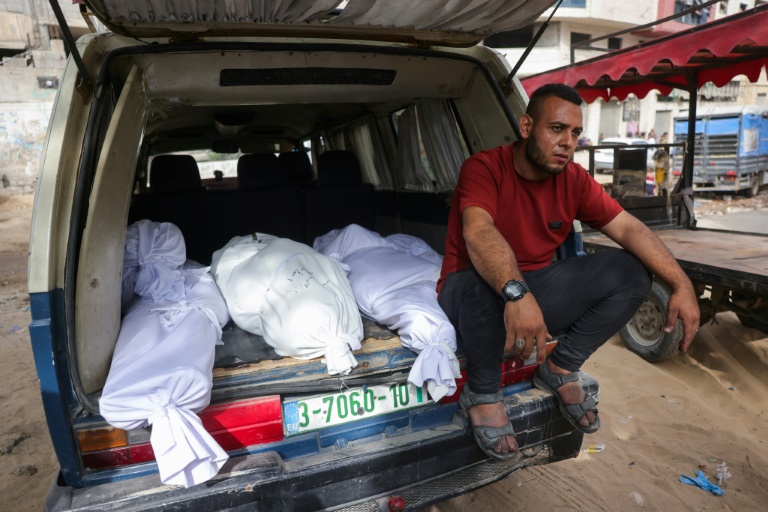 Un Palestinien est assis à côté de corps enveloppés de draps blancs à l'arrière d'une camionnette devant l'hôpital Al-Chifa à Gaza-ville, le 18 mai 2025