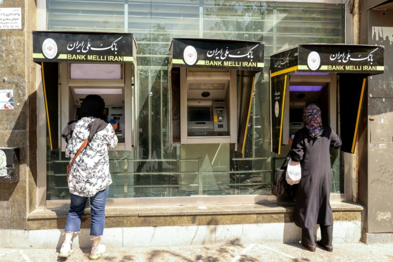 Des passantes retirent de l'argent à un distributeur de billets dans une rue de Téhéran, le 28 septembre 2025 en Iran