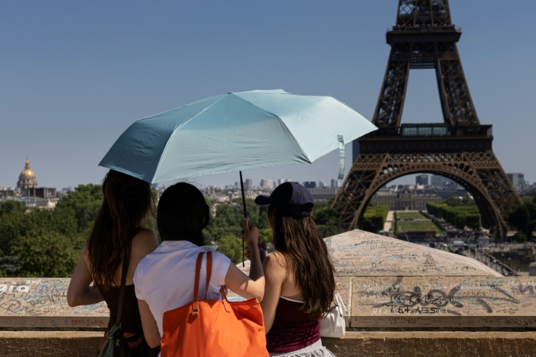 Des touristes se protègent du soleil sous un paraplluie devant la Tour Eiffel lors d'une vague de chaleur à Paris, le 27 mai 2026