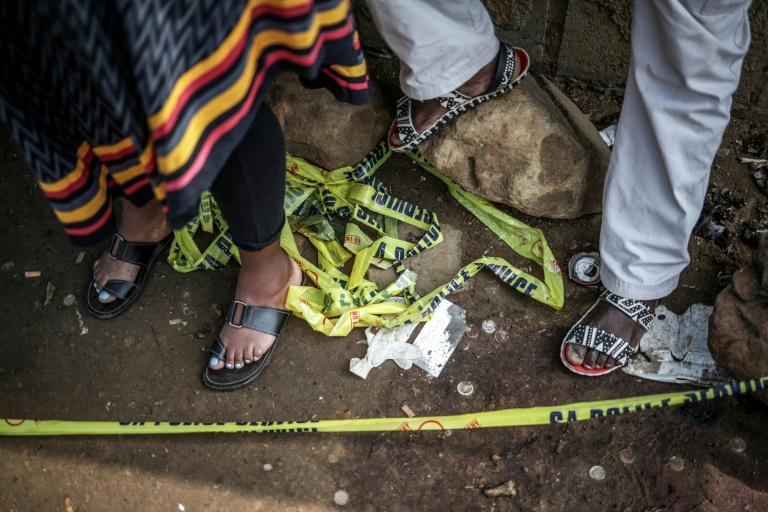 Des habitants derrière un cordon policier près du lieu de la fusillade dans un bar de l'ouest de Johannesburg qui a fait 17 morts et 15 blessés, le 27 septembre 2026  