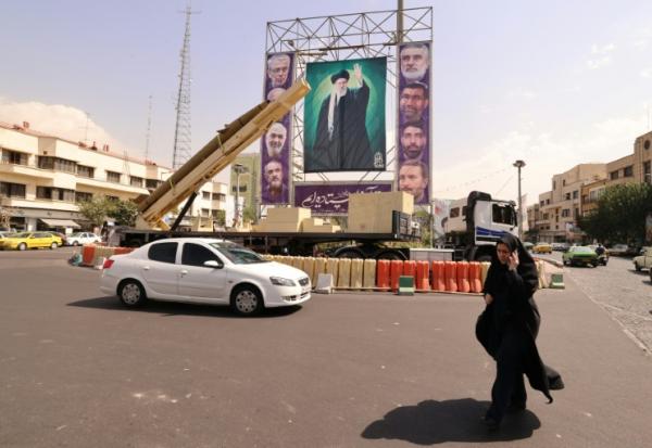 Une femme marche à côté d'un missile désactivé et devant un portrait géant du guide suprême iranien, l'ayatollah Ali Khamenei, à Téhéran le 27 septembre 2025.

