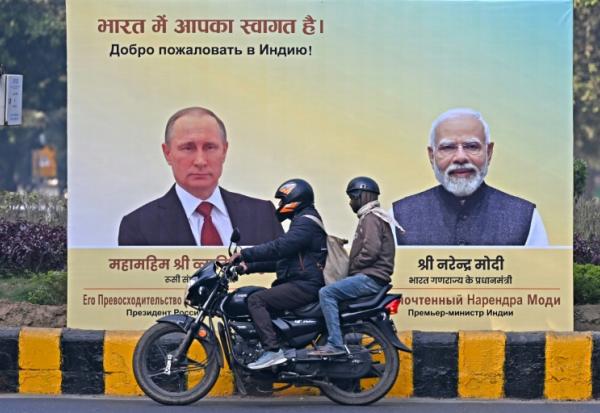 Un motard passe devant des portraits du président russe Vladimir Poutinen, à gauche, et du Premier ministre indien Narendra Modi, à droite, à New Delhi le 4 décembre 2025