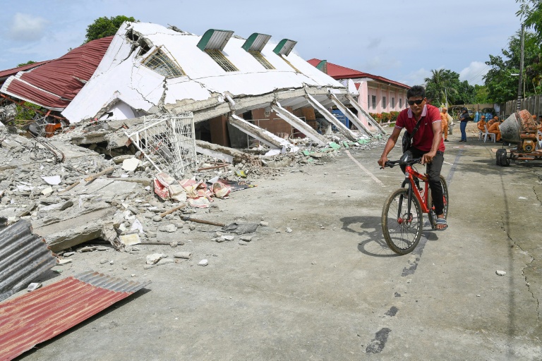 Un homme passe à vélo devant un bâtiment effondré où trois personnes ont été retrouvées mortes après un séisme à Bogo, dans la province de Cebu aux Philippines, le 2 octobre 2025