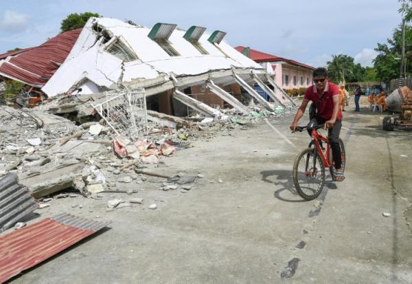 Un homme passe à vélo devant un bâtiment effondré où trois personnes ont été retrouvées mortes après un séisme à Bogo, dans la province de Cebu aux Philippines, le 2 octobre 2025