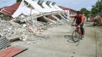 Un homme passe à vélo devant un bâtiment effondré où trois personnes ont été retrouvées mortes après un séisme à Bogo, dans la province de Cebu aux Philippines, le 2 octobre 2025