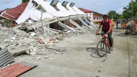 Un homme passe à vélo devant un bâtiment effondré où trois personnes ont été retrouvées mortes après un séisme à Bogo, dans la province de Cebu aux Philippines, le 2 octobre 2025
