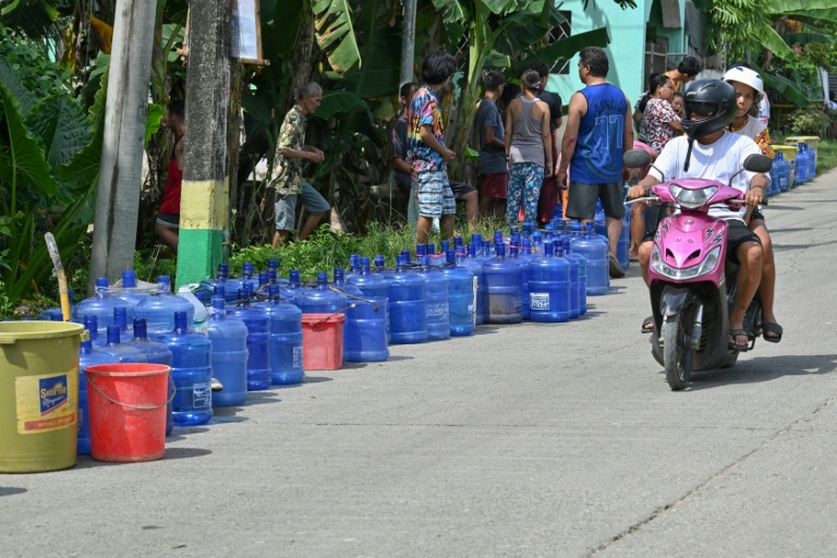 Une moto passe devant une file de bombonnes en plastique placées par des habitants qui attendent des livraisons d'eau dans la ville de Bogo, dans la province de Cebu aux Philippines, le 2 octobre 2025