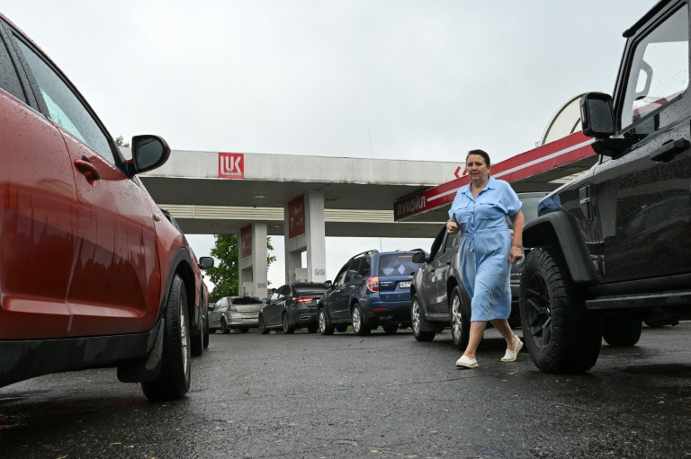 Une femme marche au milieu d'une file de véhicules dans une station-service à Vologda, en Russie, le 14 juillet 2026