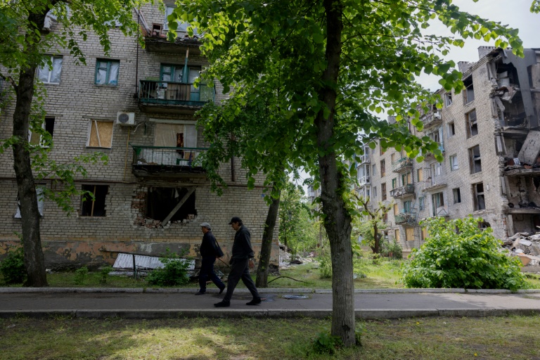 Deux hommes marchent près de bâtiments endommagés à Lyman, dans l'est de l'Ukraine, près de la ligne de front, le 7 mai 2025