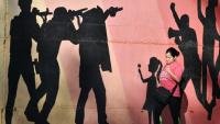 Une femme passe devant une fresque murale représentant des hommes armés visant des manifestants, allusion à la répression policière, dans une avenue de Tegucigalpa, le 27 novembre 2025