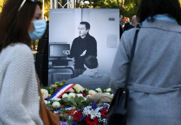 Des personnes passent devant une photographie de Samuel Paty lors d'une cérémonie hommage organisée à Eragny-sur-Oise, au nord-ouest de Paris, le 16 octobre 2021