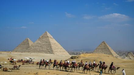 Des touristes à dos de chameau visitent la nécropole des pyramides de Gizeh, le 7 novembre 2025 en Egypte