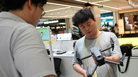 Un employé (à droite) d'un magasin dans un centre commercial inspecte un drone apporté par son propriétaire à Pékin le 16 septembre 2026.