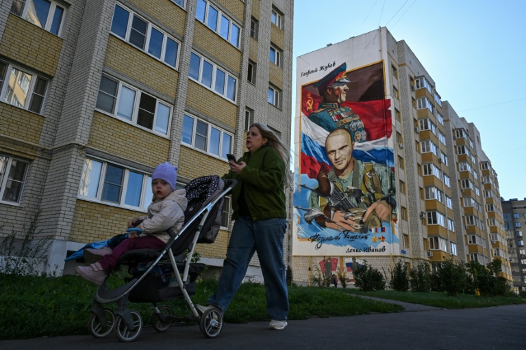 Une mère de famille passe devant une fresque représentant un colonel de l'armée russe et un ancien ministre de la Défense de l'Union soviétique, à Tambov, en Russie, le 9 septembre 2026