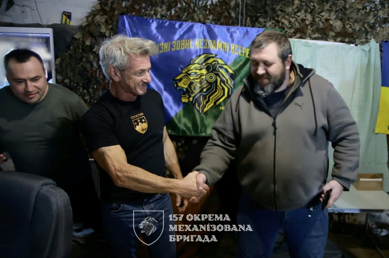 Cette photo, diffusée le 18 mars 2026 par le service de presse de la 157e brigade mécanisée indépendante ukrainienne, montre l'acteur américain Sean Penn (à gauche) posant avec les officiers lors de sa visite à la brigade, dans un lieu tenu secret de la ligne de front