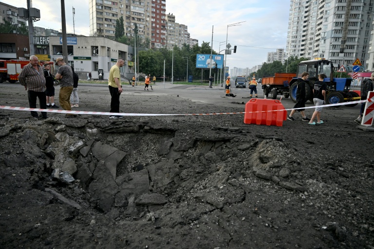 Des habitants de Kiev passent près d'un cratère causé par une frappe de missile russe sur la capitale de l'Ukraine, le 11 juillet 2026