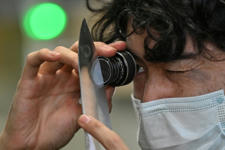 Un employé du fabricant japonais de couteaux Sumikama inspecte une lame à l'aide d'une loupe dans son usine de Seki, au Japon, le 22 juillet 2025