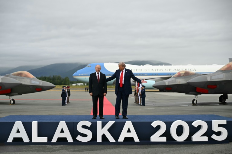 Le président américain Donald Trump et le président russe Vladimir Poutine debout sur un podium sur le tarmac après être arrivés à la base militaire Elmendorf-Richardson en Alaska, le 15 août 2025