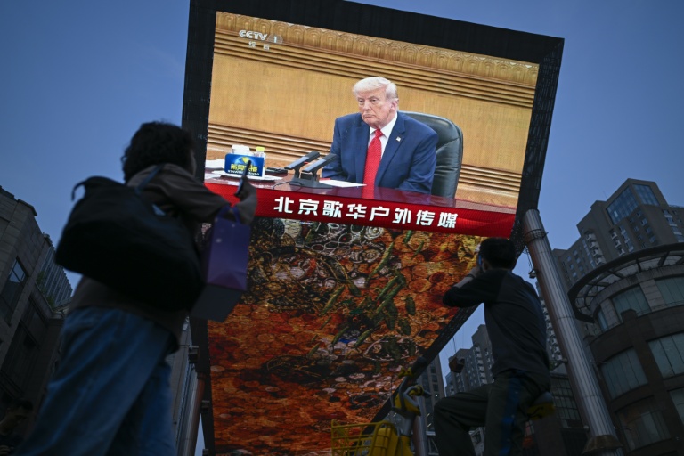 Des personnes passent devant un écran sur lequel est visible Donald Trump, le 14 mai 2026 à Pékin
