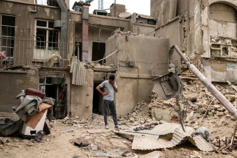 Un homme au téléphone devant des habitations détruites, le 15 mars 2026 à Téhéran 