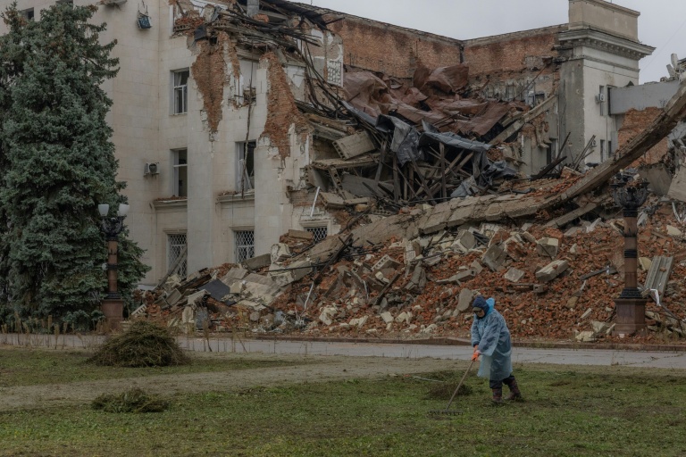 Un employé municipal ramasse de l'herbe coupée près d'un bâtiment administratif en partie détruit par une frappe russe, le 30 octobre 2026 à Kherson, dans le sud de l'Ukraine 