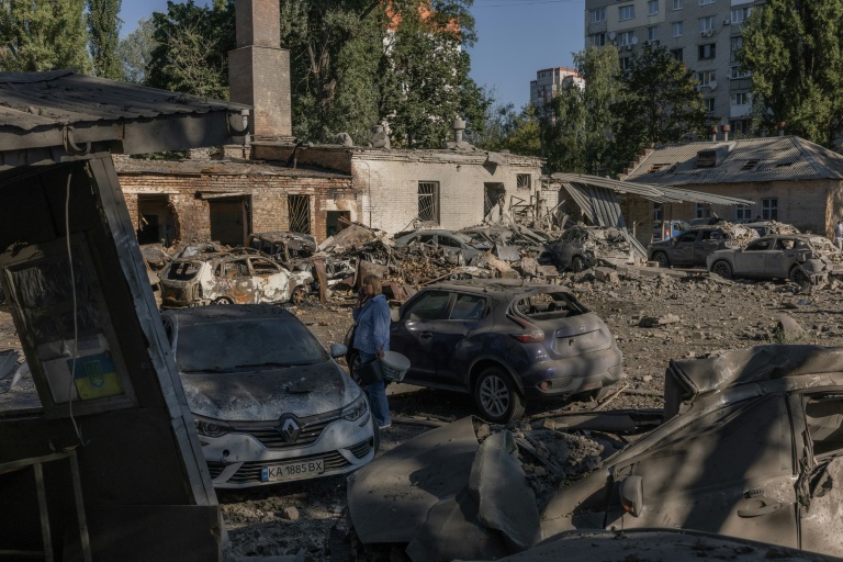 Une femme se tient près de voitures détruites et de bâtiments endommagés après une frappe russe à Kiev, le 20 août 2026