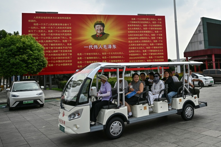 Des touristes à bord d'une voiturette électrique passent devant une fresque de Mao Zedong, place de 