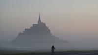 Un cycliste passe devant le Mont-Saint-Michel, enveloppé par la brume matinale, le 9 juillet 2025