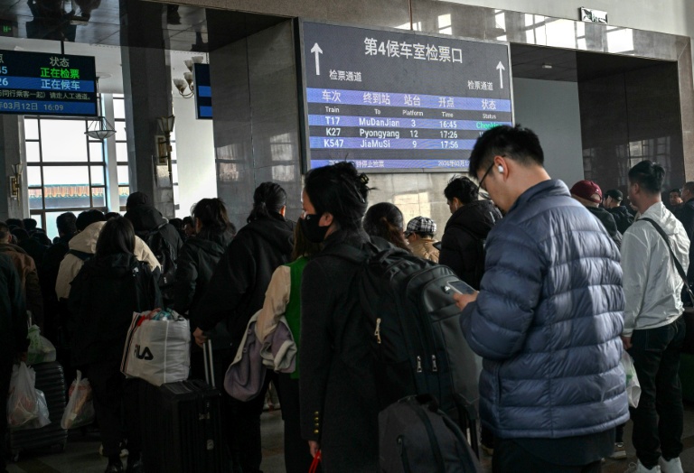 Des voyageurs font la queue à côté d'un panneau indiquant le train K27 à destination de Pyongyang, à la gare de Pékin, le 12 mars 2026 en Chine