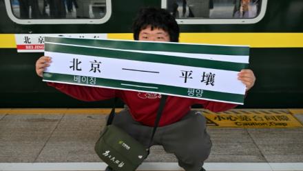 Un homme brandit une banderole "Pékin-Pyongyang" devant le train K27 à destination de Pyongyang, à la gare de Pékin, le 12 mars 2026 en Chine