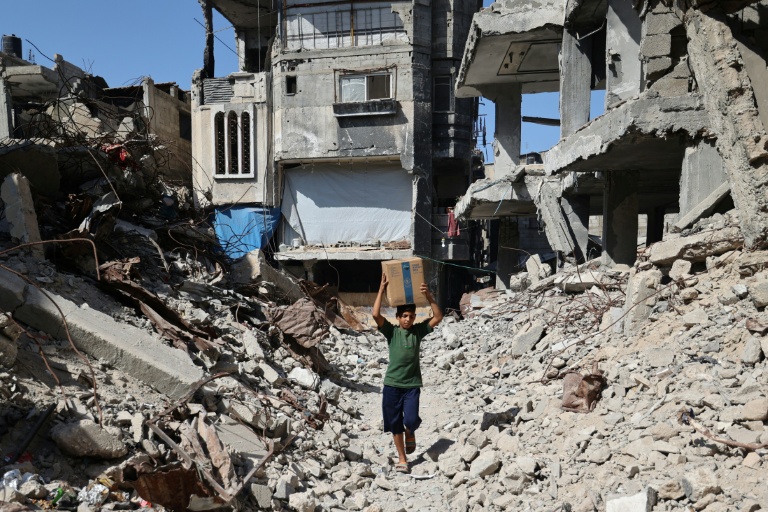 Un garçon palestinien déplacé porte une boîte de fournitures d'urgence fournies par le Programme alimentaire mondial (PAM) après l'avoir reçue d'un point de distribution d'aide au camp de réfugiés de Nuseirat dans le centre de la bande de Gaza, le 19 octobre 2025