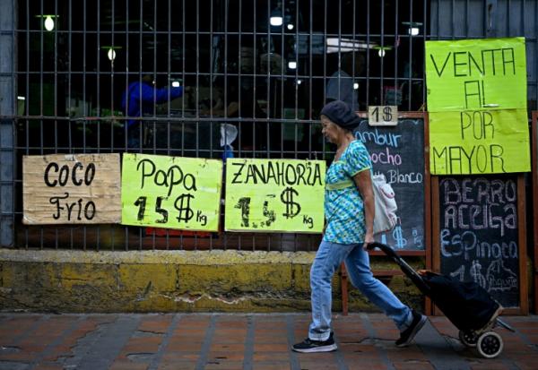 Une femme tire un chariot de courses à roulettes devant un supermarché qui affiche sur des panneaux les prix des aliments en dollars américains à Caracas, le 22 avril 2026