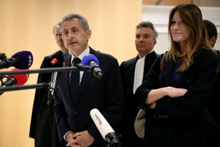 L'ancien président Nicolas Sarkozy (g), au côté de son épouse Carla Bruni (d), devant la presse dont Mediapart (micro rouge), au tribunal de Paris, le 25 septembre 2025