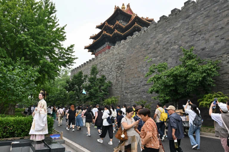 Une femme en robe traditionnelle (g) pose pour une photo alors que des touristes visitent la Cité Interdite à Pékin, le 11 juillet 2026